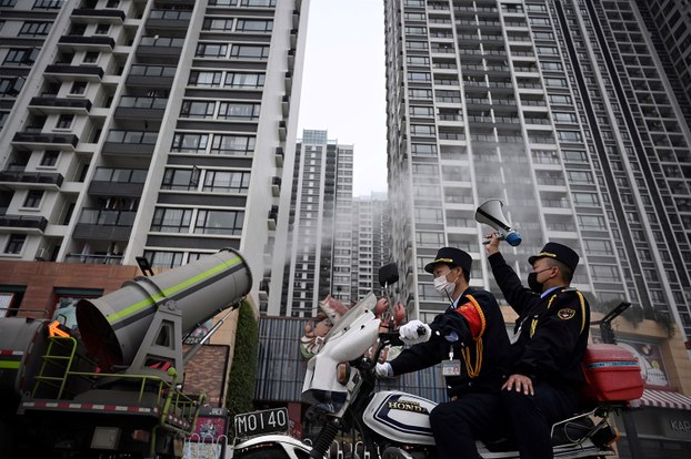 2020年2月11日，广州番禺祈福新村小区爆发新型冠状病毒后，一名男子坐在摩托车上，举喇叭宣传普及疫情防治，左边的一辆消毒车为居民楼附近的公共场所消毒。.jpeg